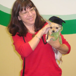 A smiling customer holding her chihuahua (which is wearing a graduation cap).